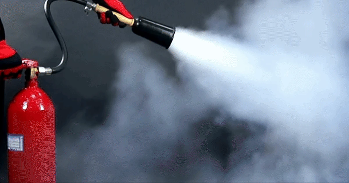 A gloved hand operating a red fire extinguisher