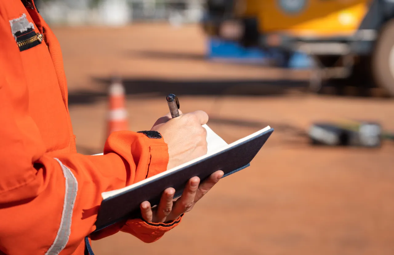 A worker in orange high-visibility clothing writing on a tablet on site