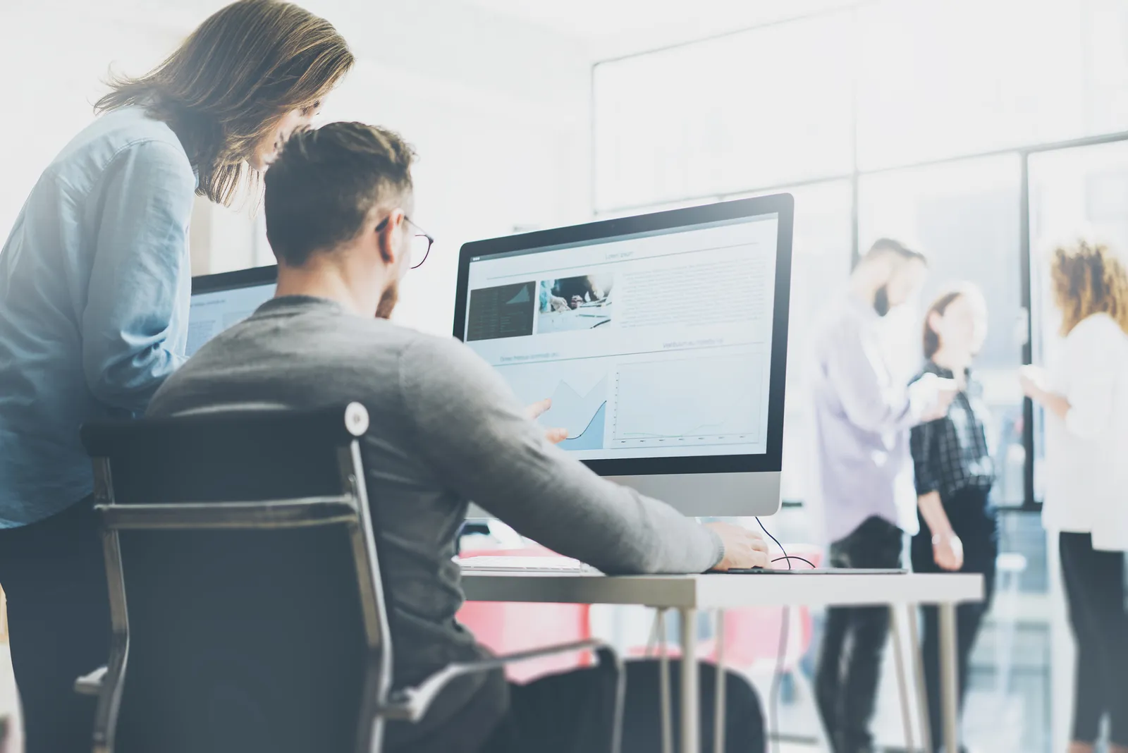 Two colleagues at a desk looking at a monitor in an office